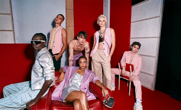 Eine Gruppe von weiblichen und männlichen Models posiert stehend oder sitzend vor einem rot-grauen Hintergrund (Foto)