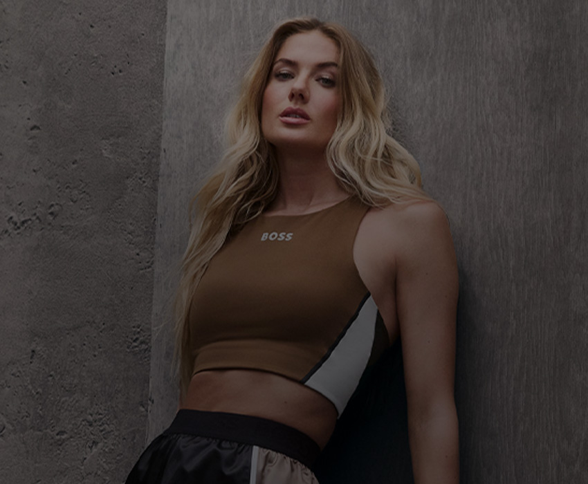 Functional Capsule collection – blonde model poses leaning against a wall in sportswear, zoomed in (photo)